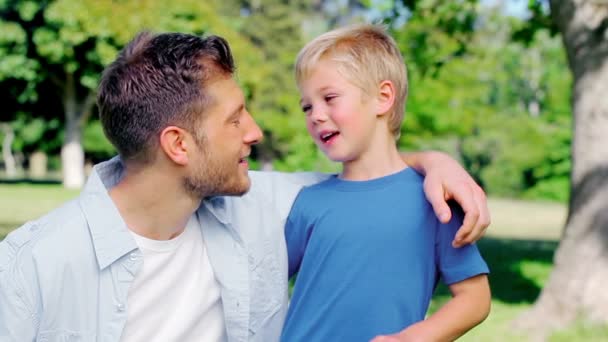 Chico discutiendo con su padre mientras se abrazan en un parque — Vídeo de stock