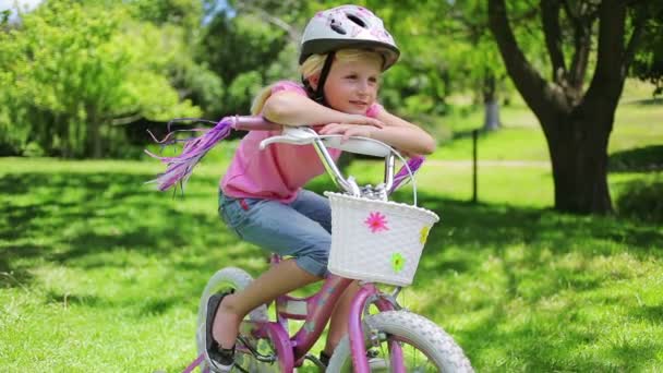 En flicka sitter på en cykel när du lutar på styret som dess tofsar blåser i vinden — Stockvideo