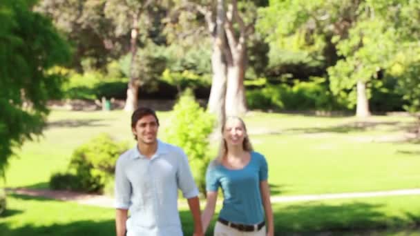 Um casal caminha em direção à câmera juntos e depois ri e acena nele — Vídeo de Stock
