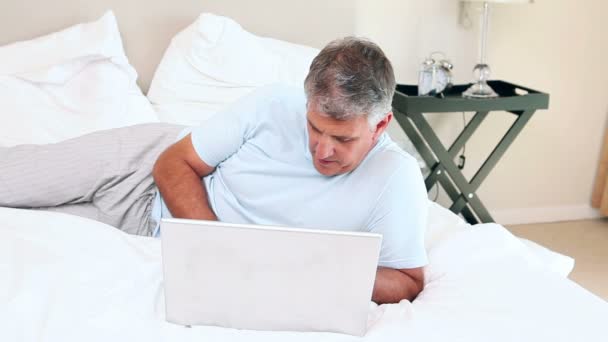 Άνθρωπος με φορητό υπολογιστή που βρίσκεται στο κρεβάτι του — Αρχείο Βίντεο