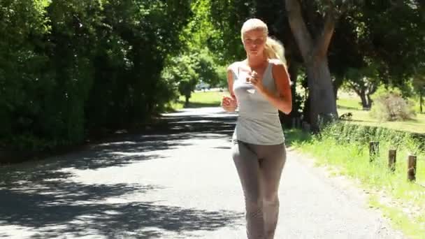 Uma mulher corre por uma estrada com a câmera na frente dela se afastando — Vídeo de Stock