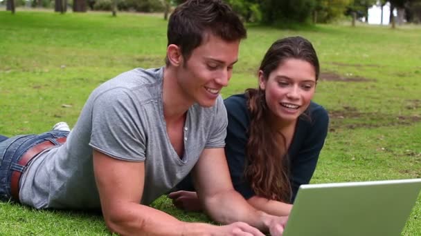 Dois amigos conversando um com o outro como eles usam um laptop enquanto deitado juntos — Vídeo de Stock