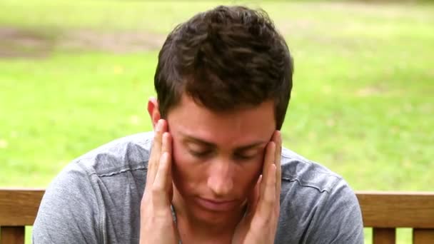 Disappointed man putting his face in his hands while shaking his head as he sits on a bench — Stock Video