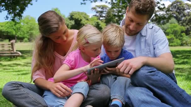 Familia sentada una al lado de la otra mientras usa una tableta PC que está siendo sostenida por los niños — Vídeos de Stock