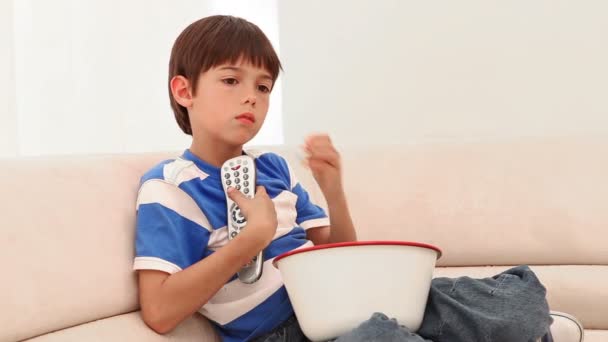 Menino comendo pipocas enquanto ele assiste televisão — Vídeo de Stock