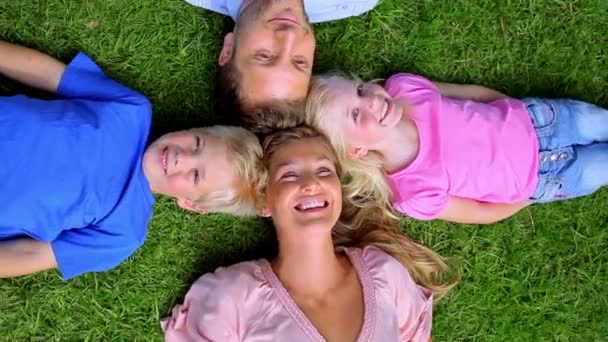 Foto aérea de una familia sonriendo mientras yacen cabeza a cabeza en la hierba — Vídeo de stock
