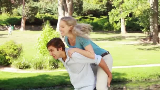 A man gives his girlfriend a piggy-back as they look at the camera — Stock Video