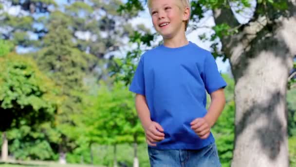 Niño saltando en un parque con los brazos levantados — Vídeo de stock