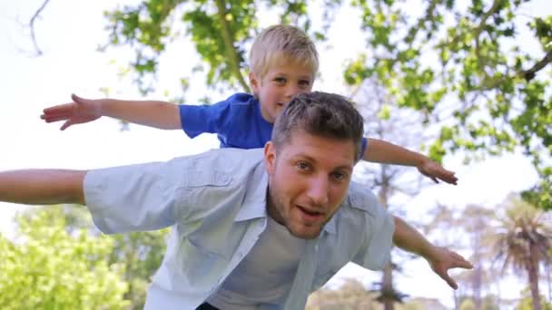 Ein Vater schwankt von einer Seite zur anderen, während er seinem Sohn ein Huckepack mit ausgebreiteten Armen reicht — Stockvideo