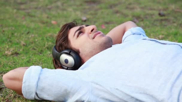 Un hombre se acuesta mientras escucha música en sus auriculares — Vídeo de stock