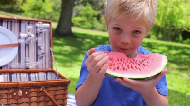 A boy looks at the camera while biting a watermelon before swallowing and smiling — Stock Video