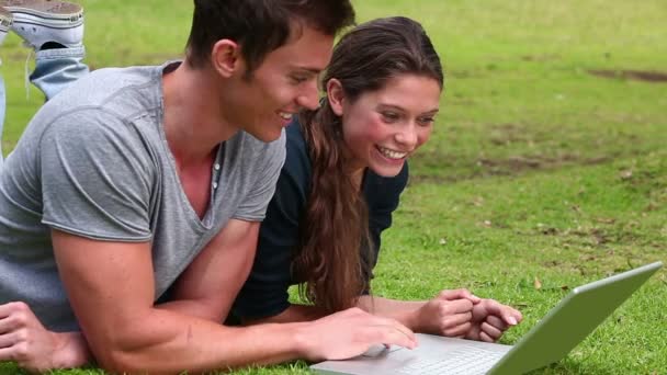 Twee vrienden lachen als de blik op een laptop terwijl naast elkaar liggen — Stockvideo