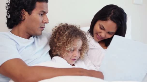 Familia con un libro sentado en su cama — Vídeos de Stock