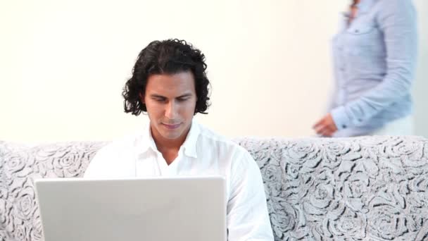 Женщина обнимает своего парня, который пользуется ноутбуком на диване — стоковое видео