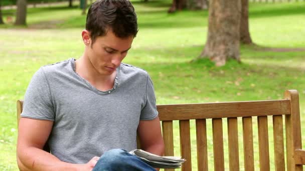 Muž čtení novin než se podíváme na kameru, jak sedí na lavičce — Stock video