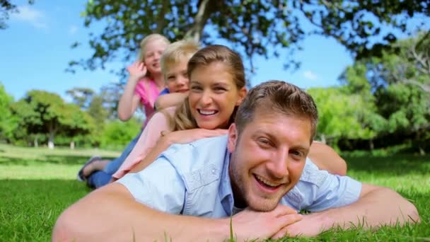 A girl waves her arm as she lies on her family who are laughing while lying on top of each other — Wideo stockowe