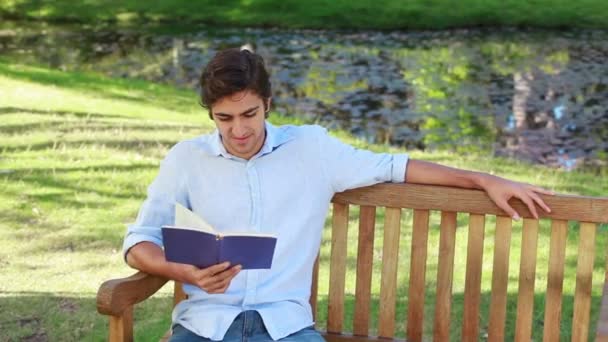 Man zit op een bankje tijdens het lezen van een boek — Stockvideo