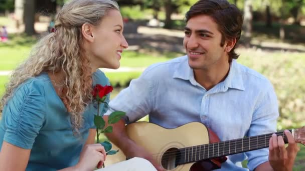 Um homem serenata sua namorada com uma música enquanto ela segura uma rosa enquanto eles olham para a câmera — Vídeo de Stock