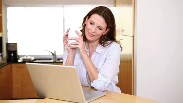 Frau trinkt einen Kaffee vor ihrem Laptop — Stockvideo