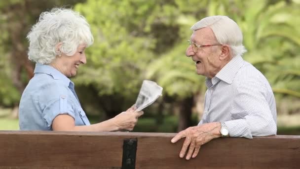 Oude paar lachen op een bankje met krant — Stockvideo