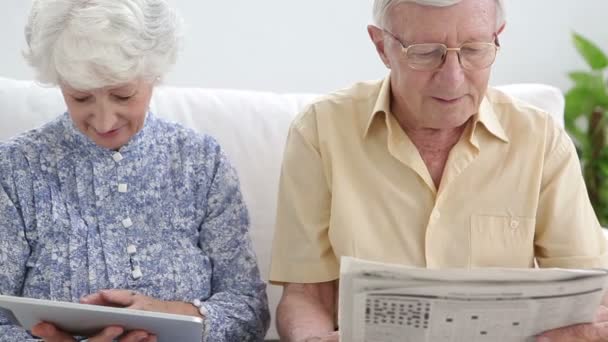 Old couple using a newspaper and a tablet — Stock Video