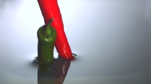 Chilipepertjes vallen in water — Stockvideo