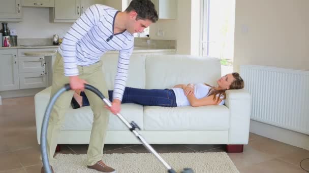 Frau schläft auf dem Sofa, während Mann die Hausarbeit erledigt — Stockvideo