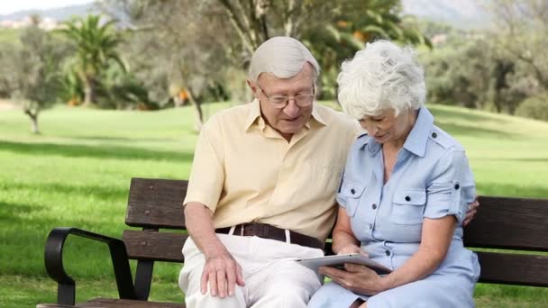 Vieux couple utilisant une tablette sur un banc — Video