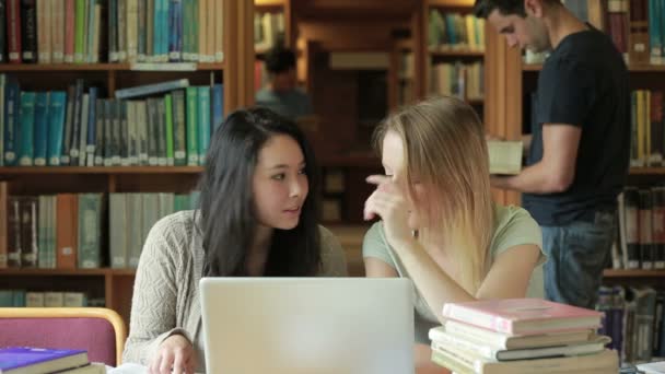 Studenten kijken iets op laptop in bibliotheek — Stockvideo