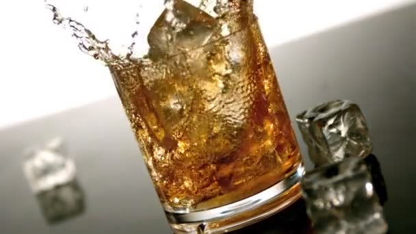 Лед падает в стакан виски и льда — стоковое видео