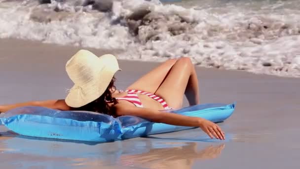 Girl sunbathing on a lilo on the beach getting splashed by the waves — Stock Video