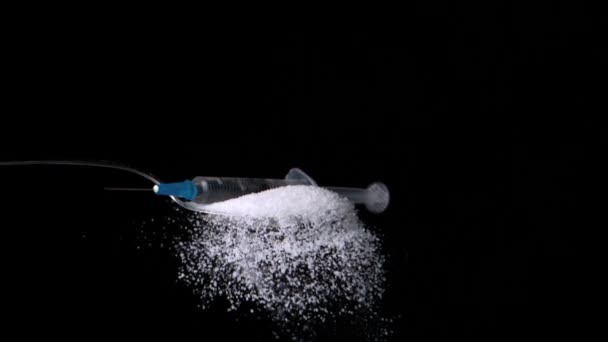 Syringe falling onto spoon full of sugar on black background — Stock Video