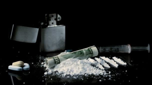 Свернутая долларовая купюра падает на груду белого наркотика со шприцем зажигалки и таблетки — стоковое видео