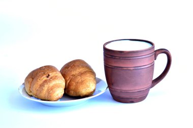 Süt ve kruvasan dolu bir kupa beyaz bir masada yatıyor..