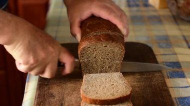 Bir adam bir somun ekmeğin parçalarını kesmek için geniş bir bıçak kullanır..