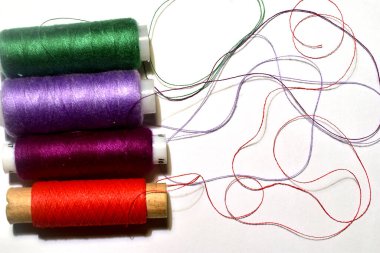 There are spools of thread of different colors on a white table.