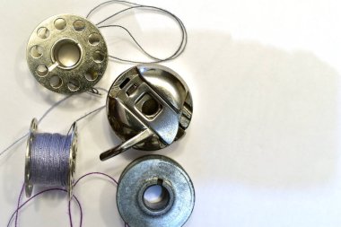 The picture shows bobbins and a sewing machine shuttle on a white table.