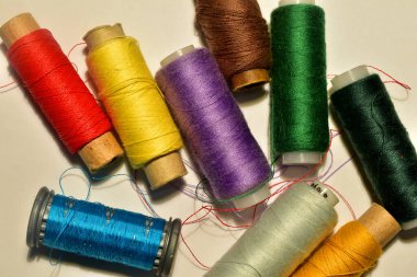 On a white table lies a set of spools of thread of different colors.