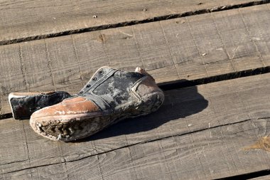 The picture shows an old, torn trainer lying on its side on old planks.