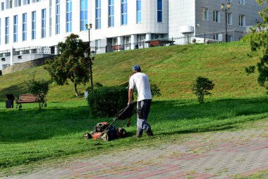 Editör imajı. Tambov. Tambov Bölgesi. - Rusya. 08 numara. 18 yaşındayım. 2021 yılı. Şehir parkında, bir işçi çimleri mekanik çim biçme makinesiyle biçiyor..