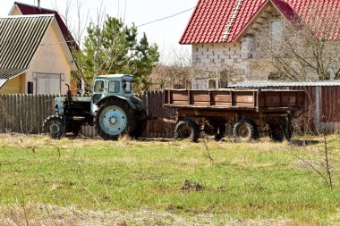 Resimde, işe hazır eski bir traktör çitin yanında duruyor..