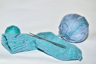 Beyaz bir arka planda örülmüş bir çorap ve mavi bir ip yumağı uzanır..