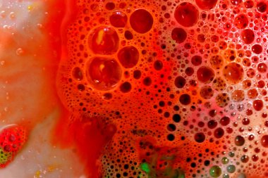 Açık kırmızı sıvı yüzey arka planında sabun baloncuklarının yakın plan görüntüsü.