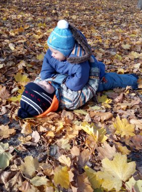 İki çocuk parkta kuru yapraklara uzanıyor, bebek ağabeyine uzanıyor ve ona bakıyor..