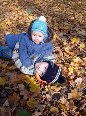 İki çocuk parkta kuru yapraklara uzanıyor, bebek ağabeyine uzanıyor..