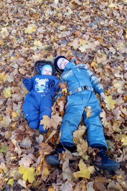 Sonbaharda parktaki kuru yapraklara uzanmış, tulum giymiş iki çocuk..