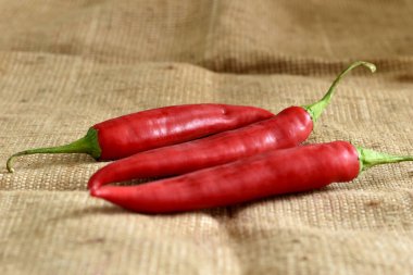 Resimde, üç kırmızı biber kaba bir kumaşın üzerinde yatıyor..
