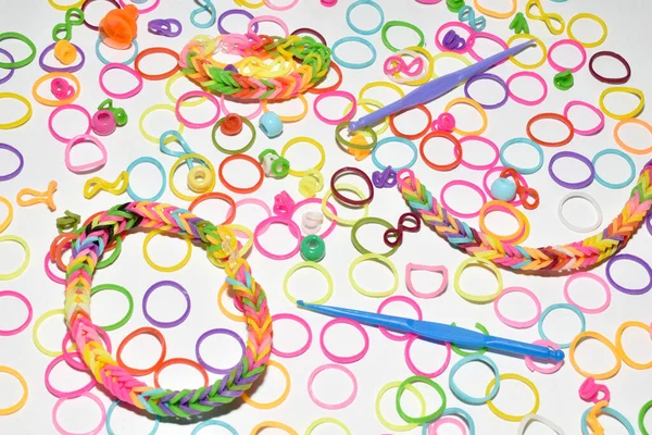 On a white background, colored elastic bands and a tool for weaving these elastic bands are scattered.