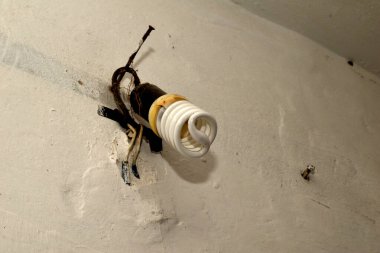 Resimde, tozlu, enerji tasarruflu bir ampul eski, kirli bir duvara asılı..