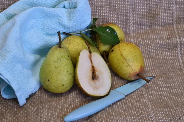 In the picture, ripe green, yellow pears and one cut in half lie next to the knife on the table.